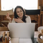 A woman smiling at a laptop during a video call in a wooden cabin