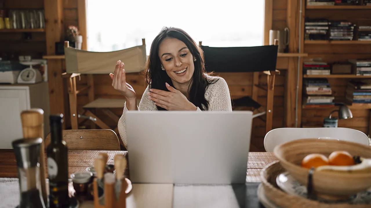 A woman smiling at a laptop during a video call in a wooden cabin