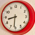 A red round wall clock on a light textured wall
