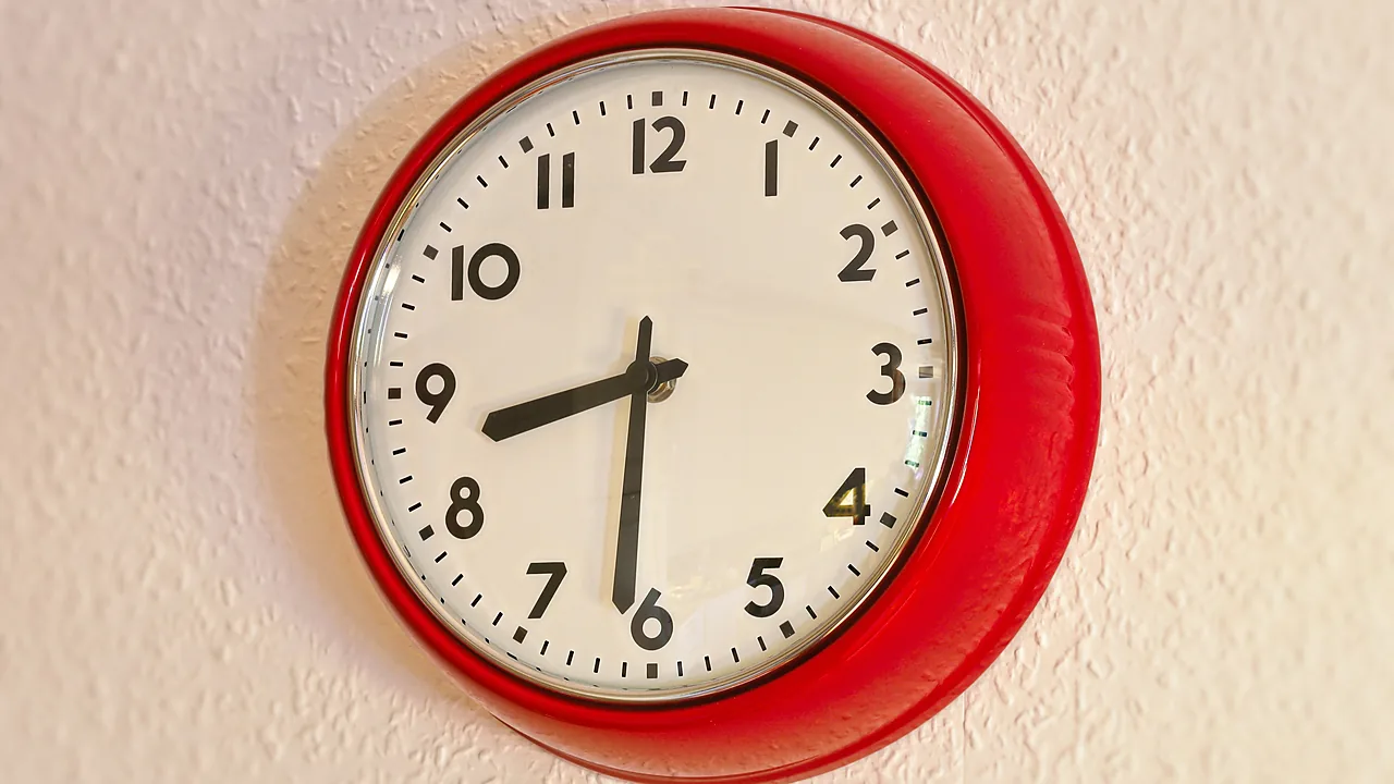 A red round wall clock on a light textured wall