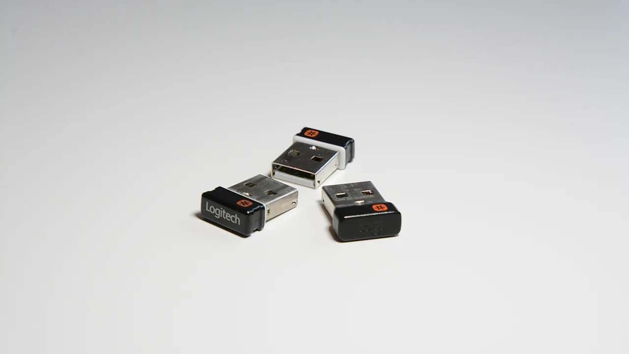 Three Logitech Unifying USB receivers on a white surface, each showing the orange Unifying logo