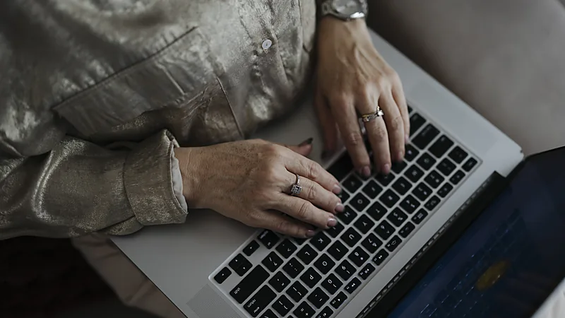 Hands with rings typing on a laptop keyboard, seen from above