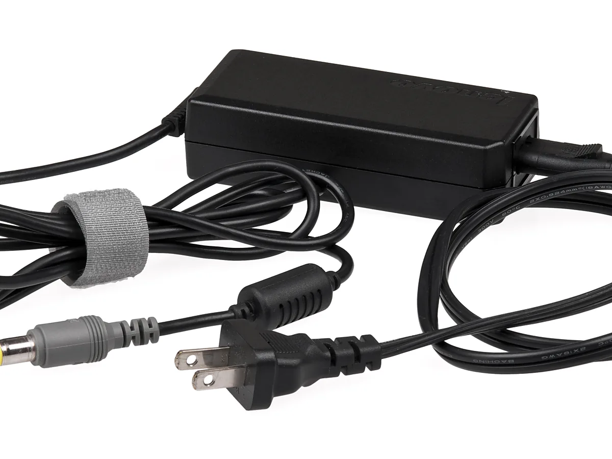 A black laptop AC adapter photographed on white, with its brick, coiled mains lead, barrel plug and two-pin wall plug all visible.