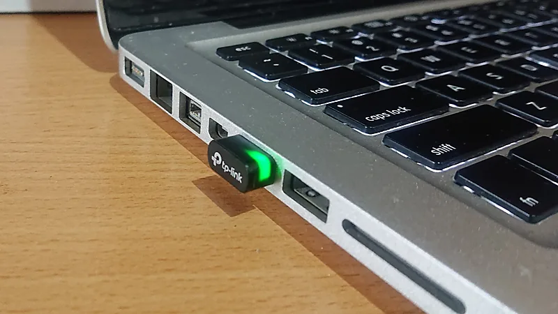 A TP-Link nano USB adapter glowing green while plugged into the side of a laptop
