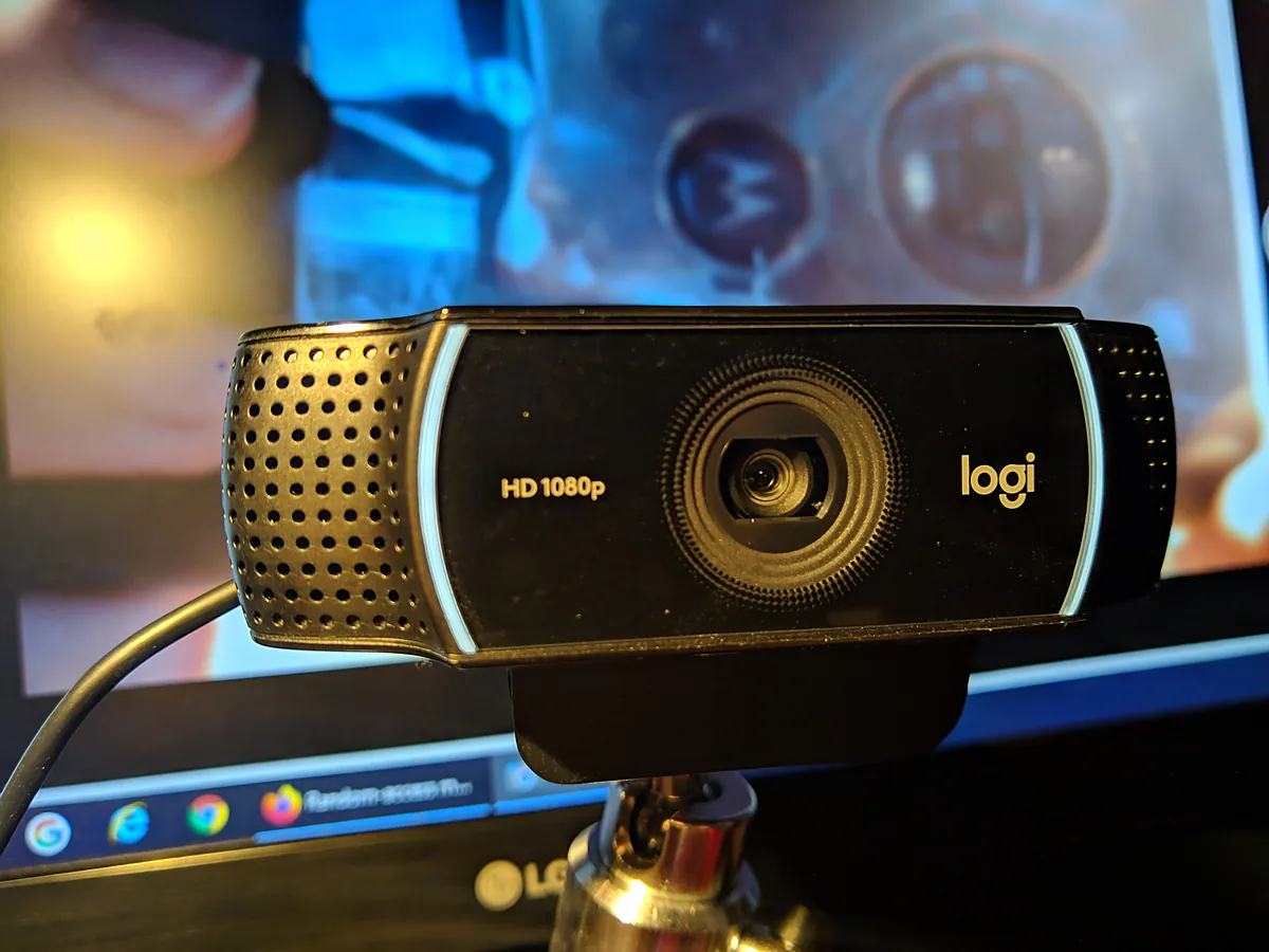 A black Logitech C922 webcam on a small tripod in front of a monitor, with its lens, dual microphone grilles and HD 1080p label visible.