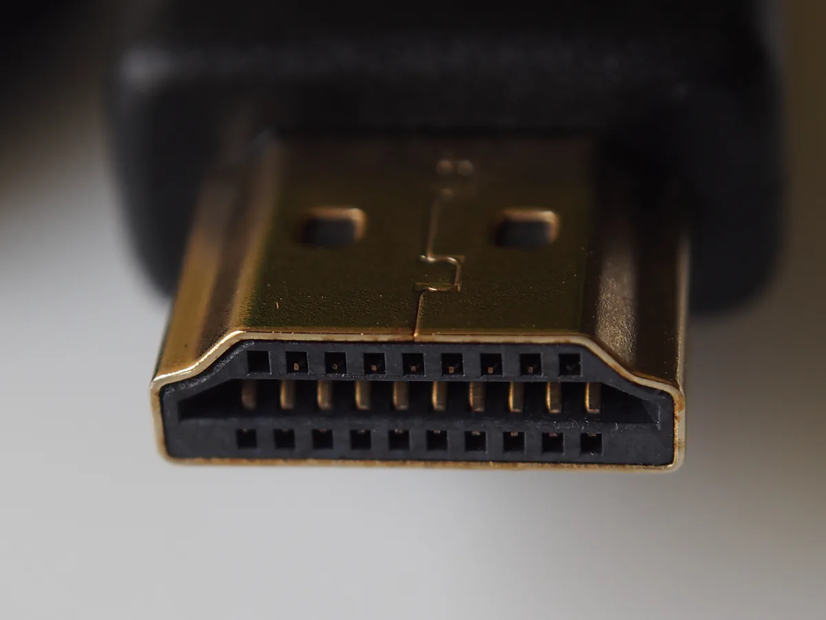 Macro photograph of the gold-plated plug on an HDMI cable, showing its trapezoid shape and the two rows of pins inside the connector.