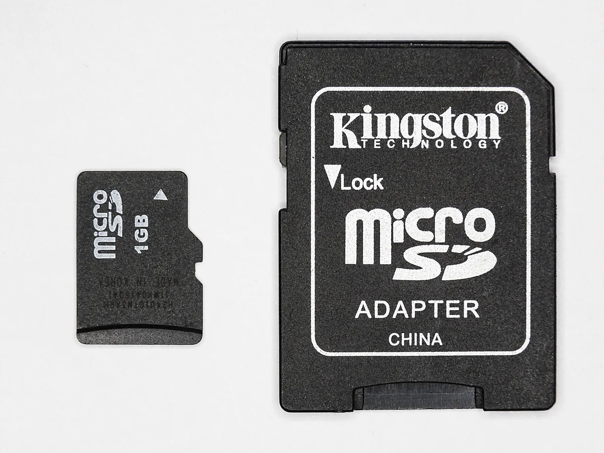 A microSD card beside its black SD adapter, with the adapter’s Lock marking and slider visible on its left edge.