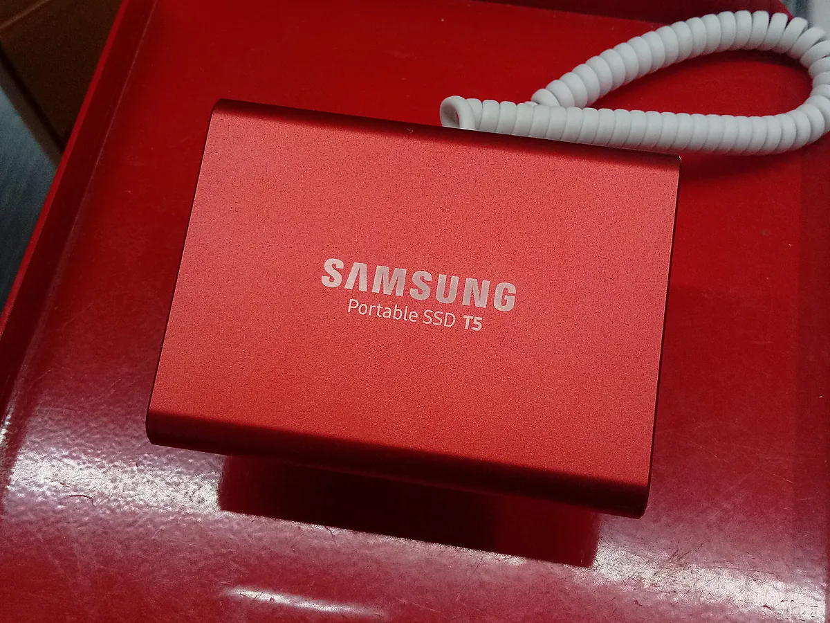A red Samsung Portable SSD T5 lying on the lid of its box, with its white coiled USB cable beside it.