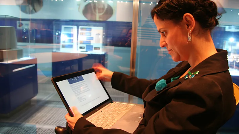 A woman holding a thin touchscreen laptop and scrolling with her thumb