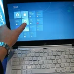 A finger tapping a tile on the touchscreen of a Windows laptop