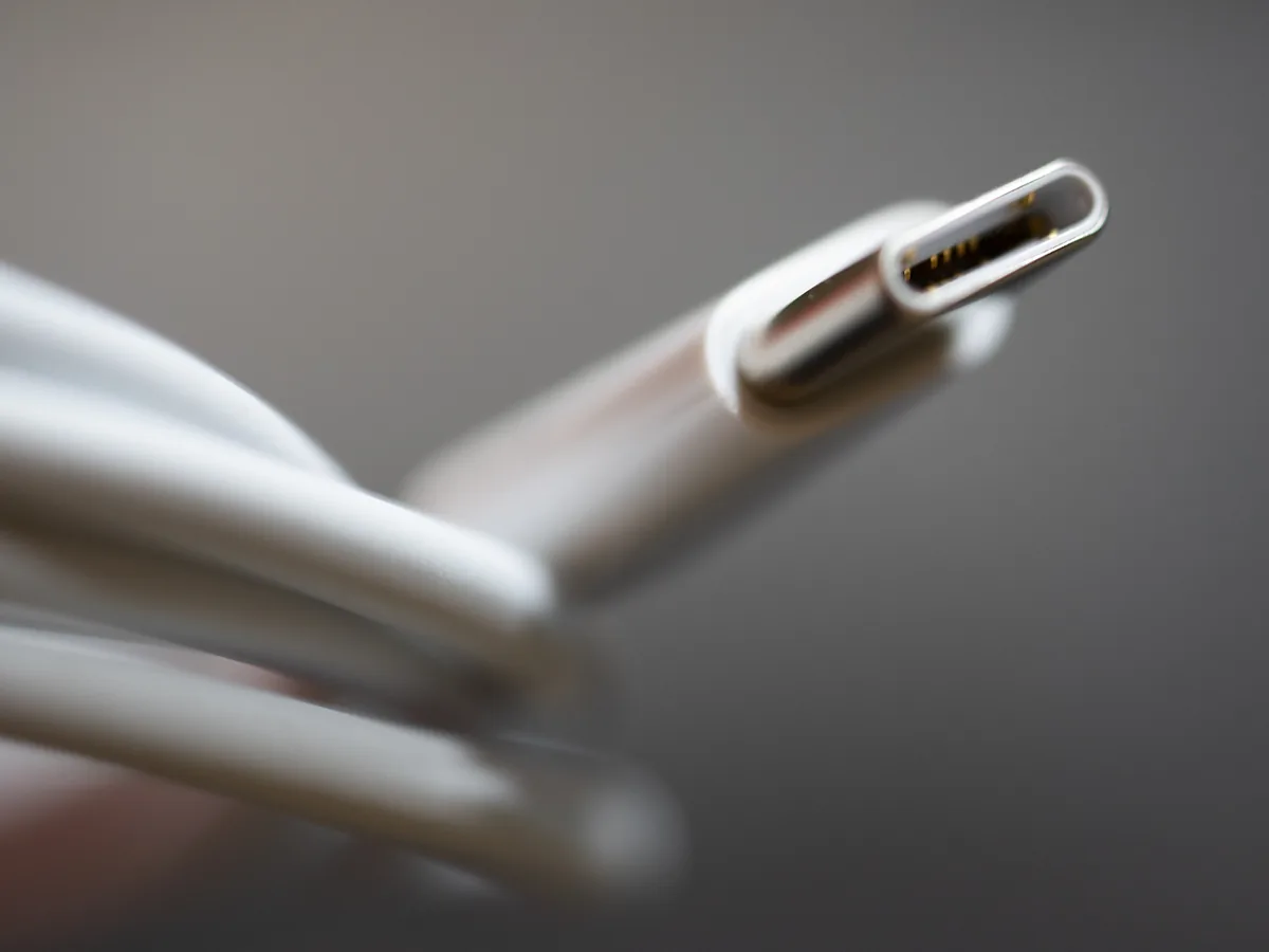 Macro photograph of the metal tip of a white USB-C charging cable, with the cable coiled out of focus behind it.