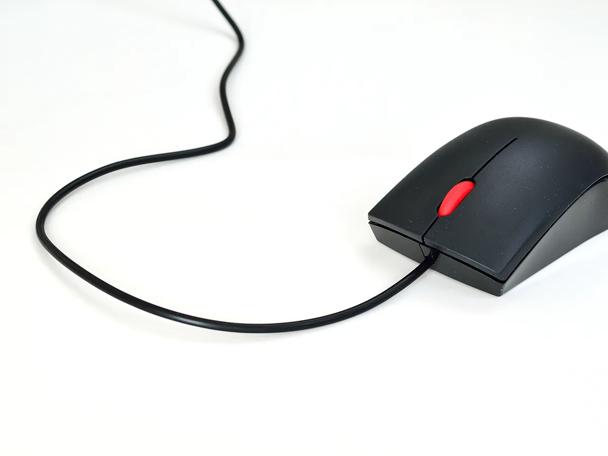 A black wired USB mouse with a red scroll wheel and its cable coiled on a white surface.
